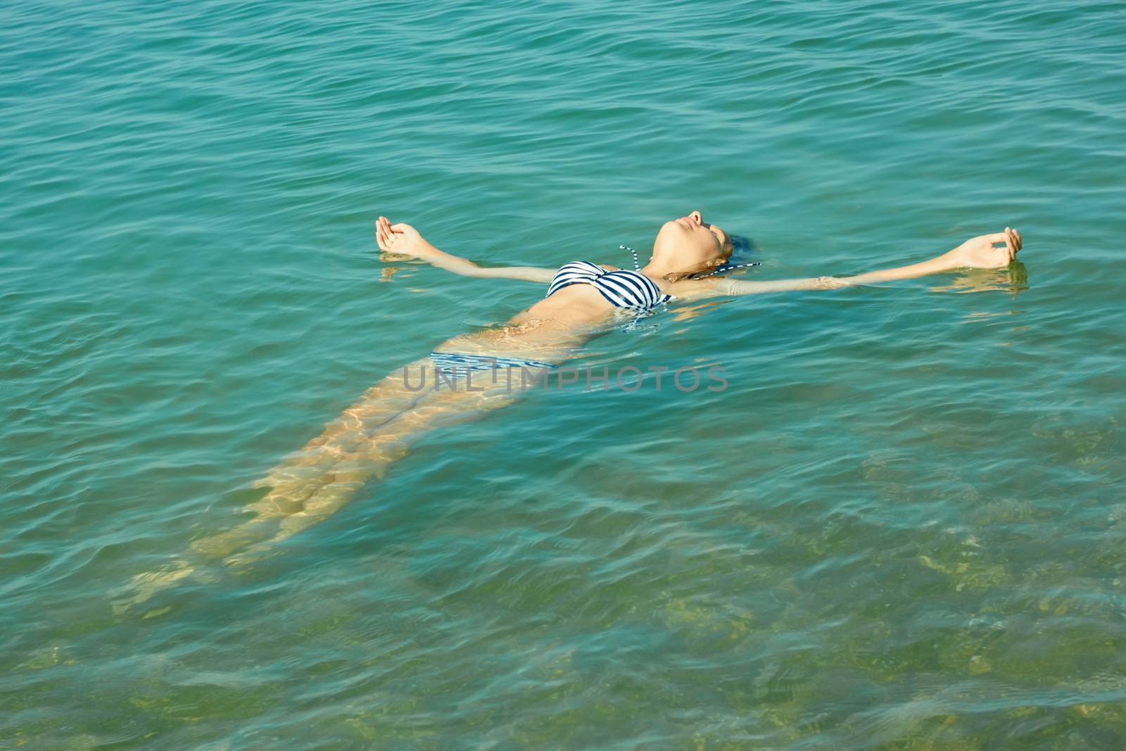 Teen girl lying on the sea water surface by qiiip