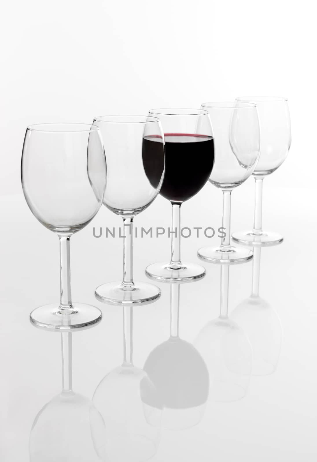 Glass of red wine in a row of empty glasses, with reflection, on white background.