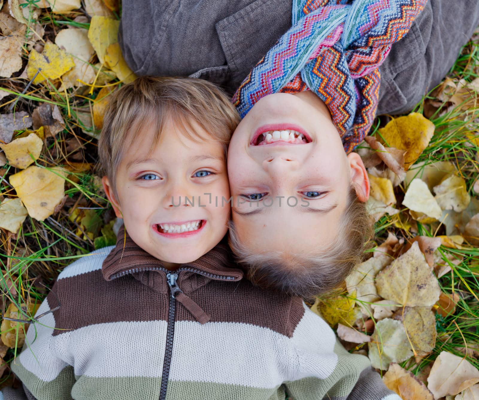 Happy kids lying on autumnal ground covered with dry leaves