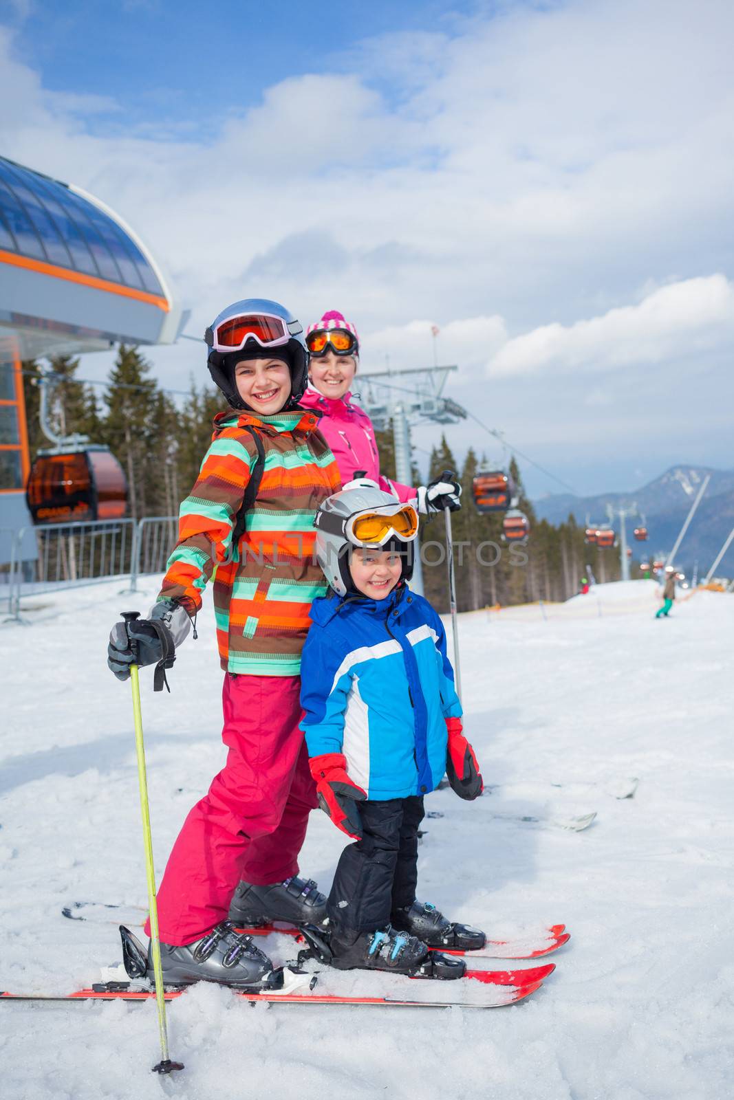 Two happy smiling kids in ski goggles and a helmet with his mother in the mountains