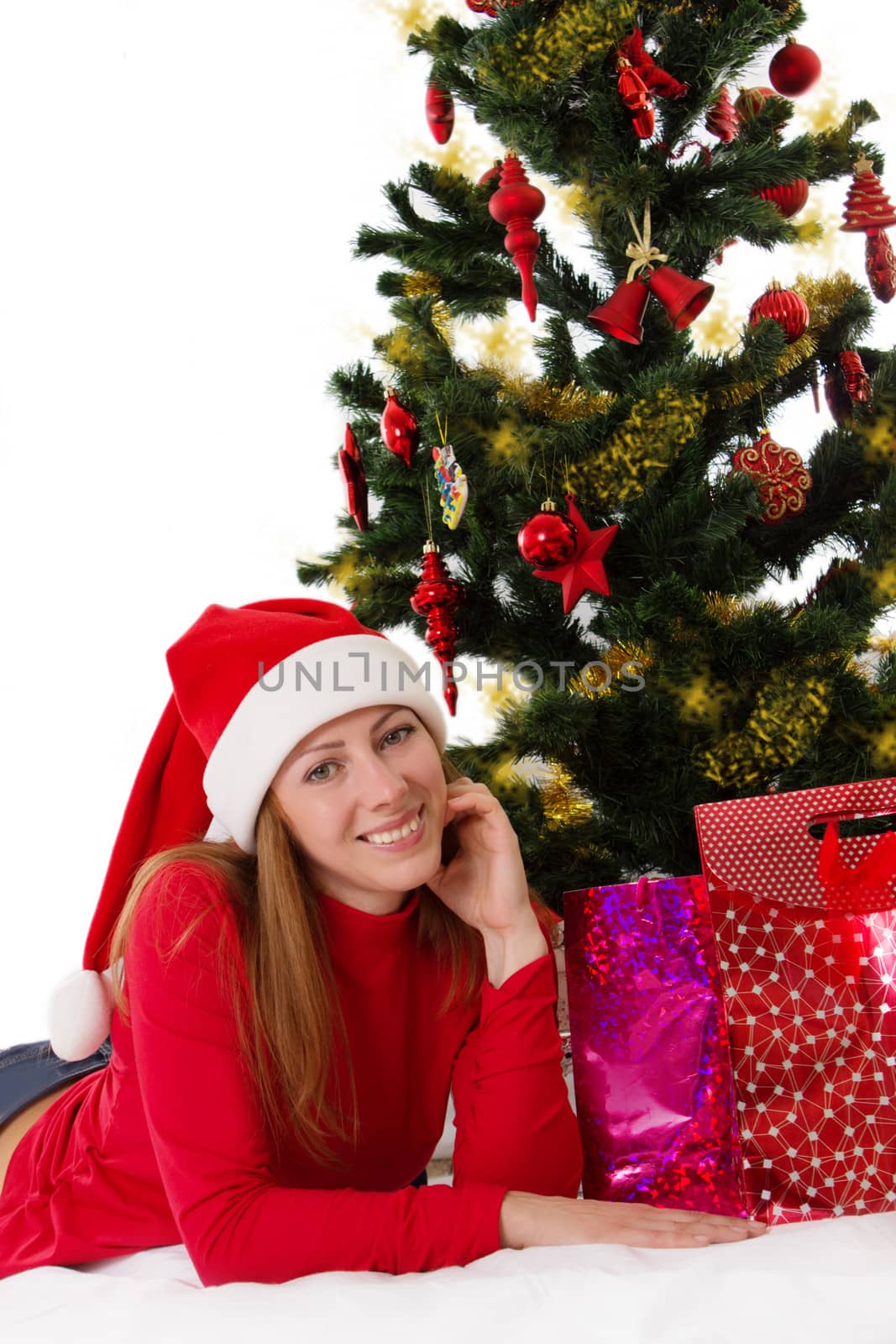 Smiling woman in red lying under Christmas tree with gifts