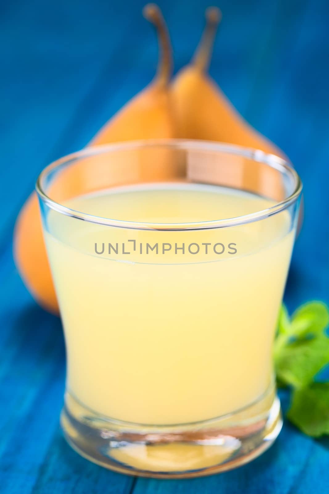 Pear juice in glass with Bosc pear in the back on blue wood (Selective Focus, Focus on the front rim of the glass)