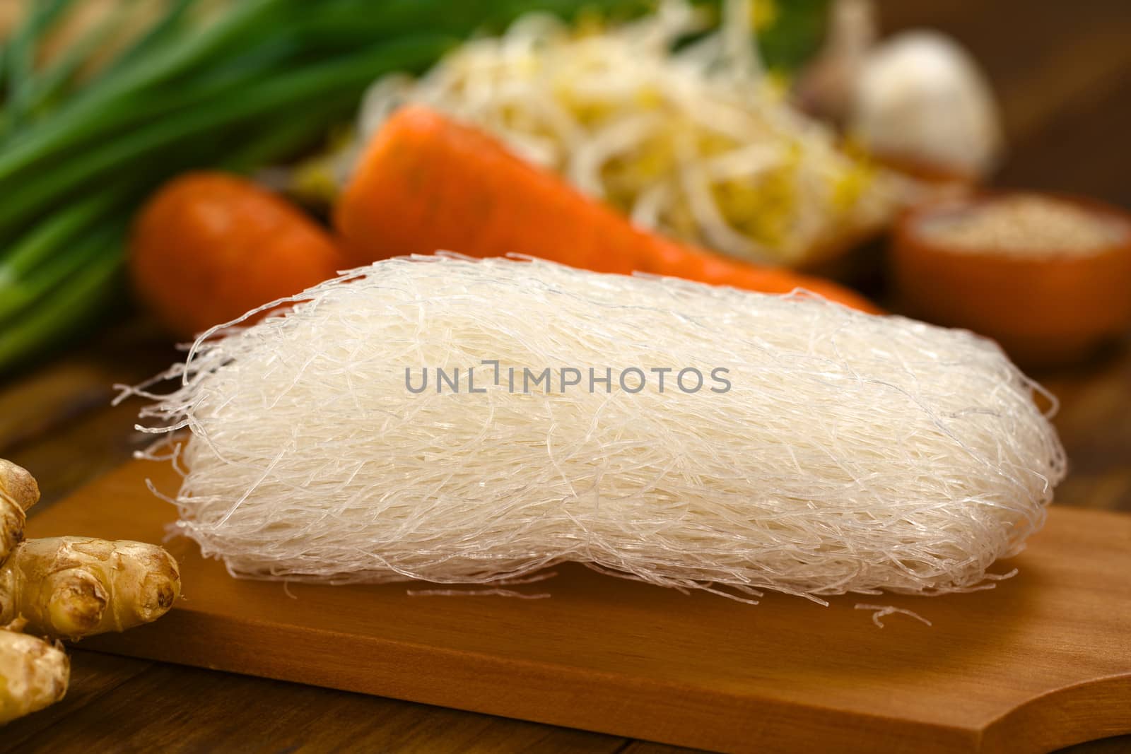 Raw rice noodles on wooden board with ginger and other vegetables (Selective Focus, Focus on the front of the noodles)