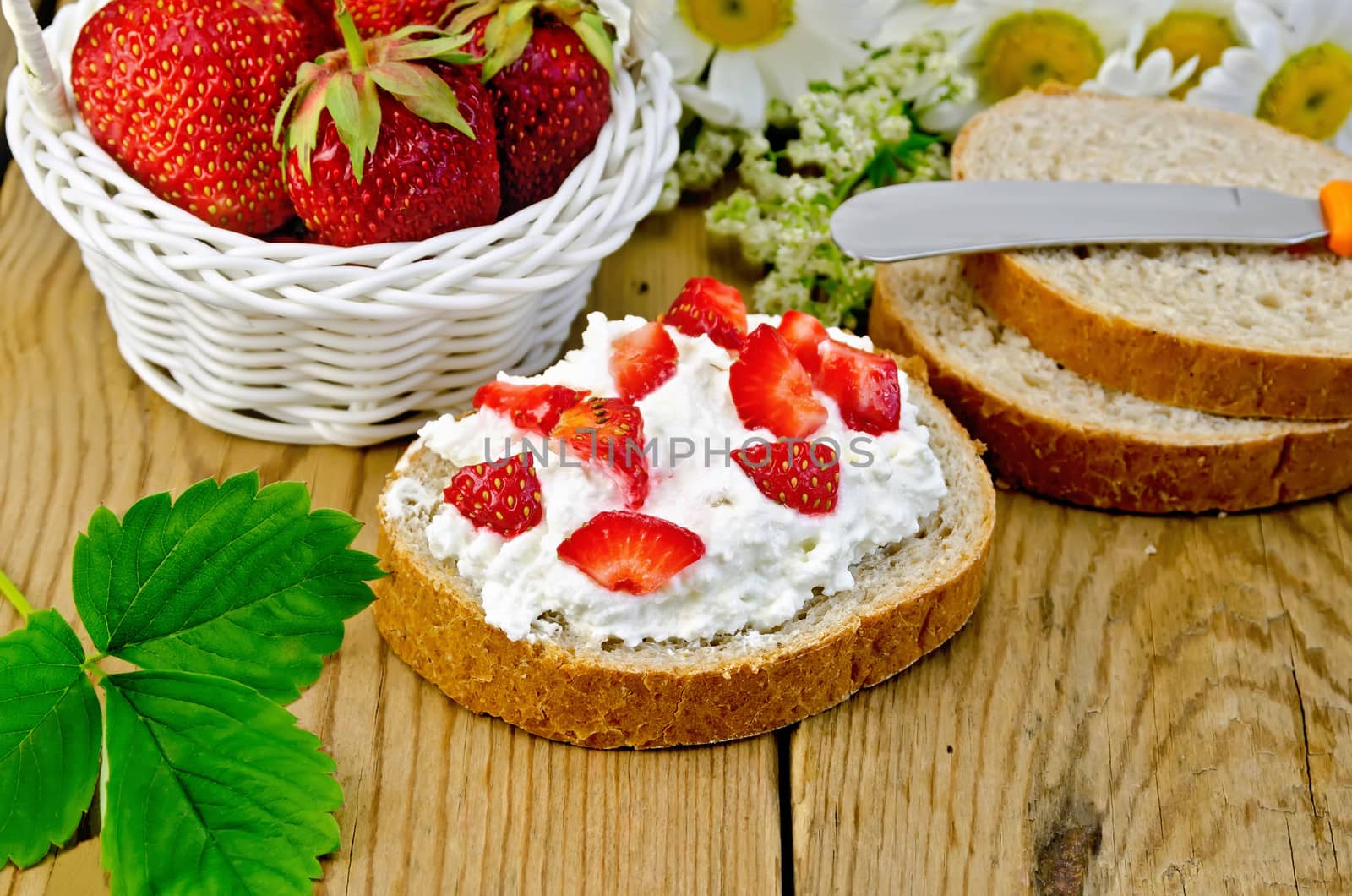 Hunk of bread with cottage cheese cream, strawberries, a basket with berries, leaf, flower daisies on a background of wooden boards