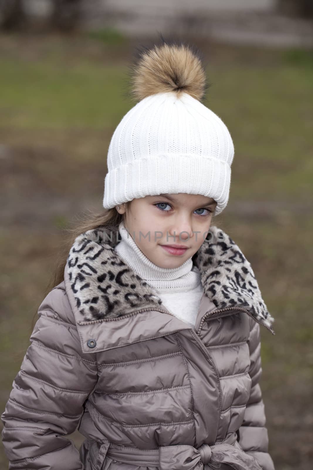 Portrait of beautiful little girl in a white knitted hat autumn