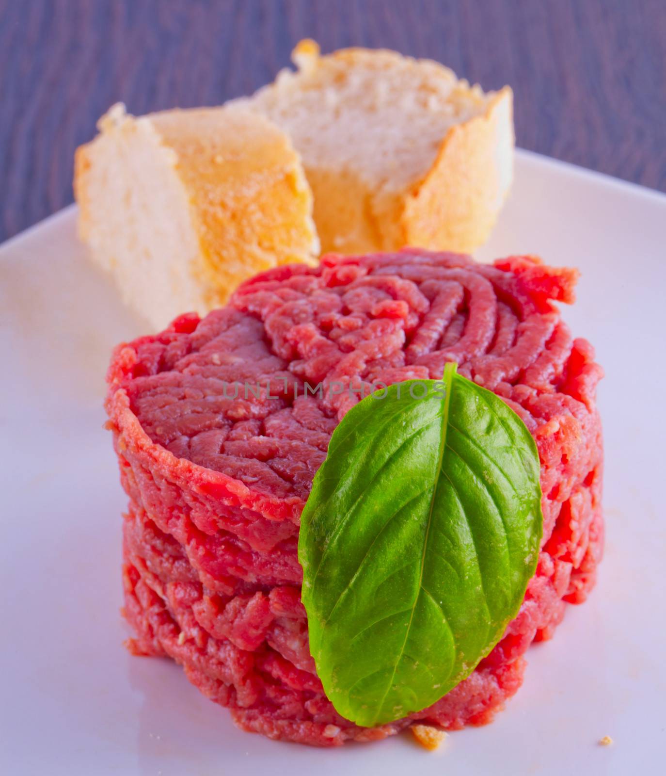 Raw meat in round shape with basil over white plate