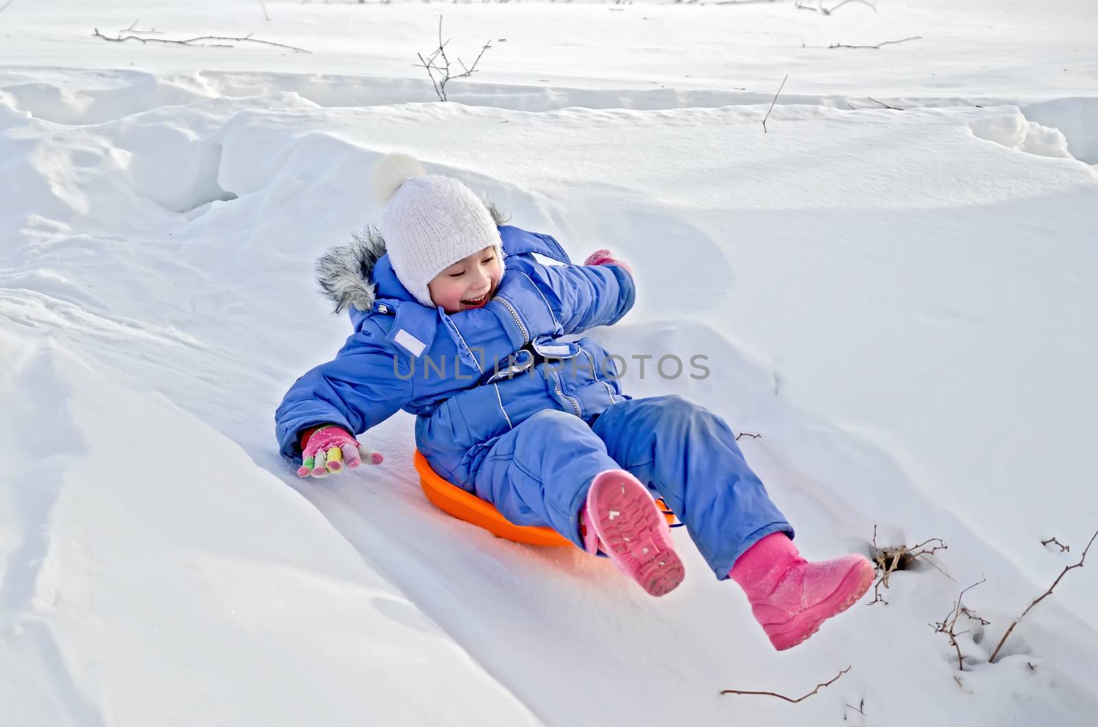 Little girl on a sled sliding down a hill in the snow in winter