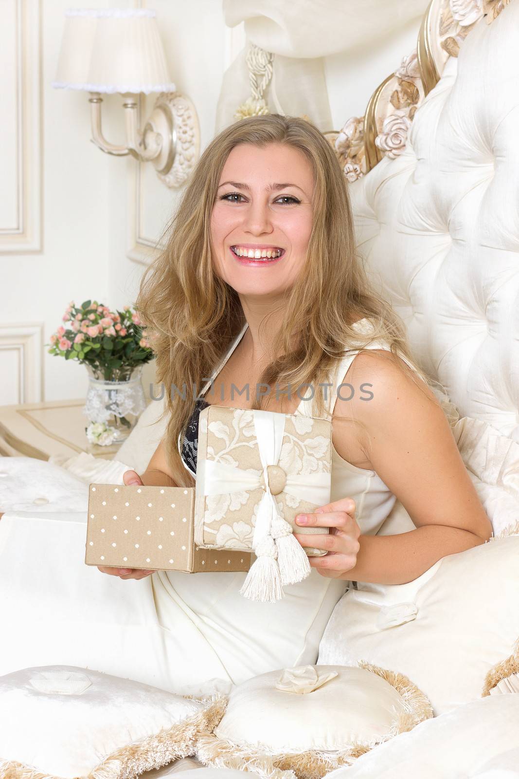 Stylish blond woman in black dress  in hotel apartment. Sexy girl gifts relaxing on bed at home luxury interior