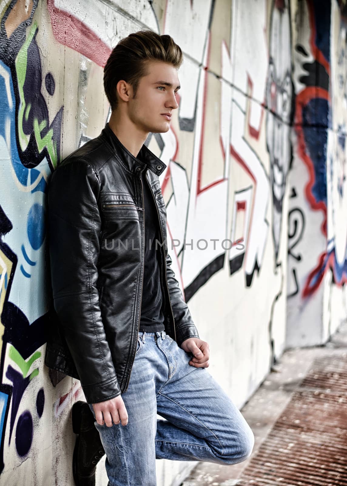 Attractive blond haired young man standing against graffiti wall