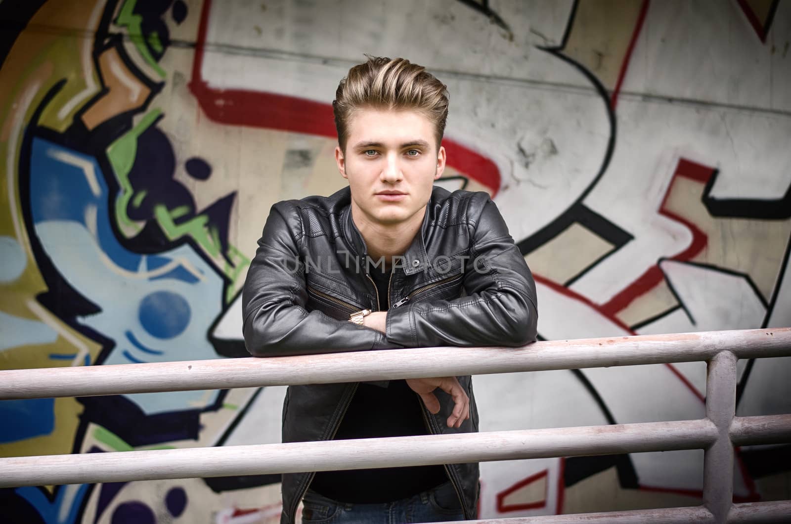 Handsome blond haired young man leaning on metal railing, in urban environment