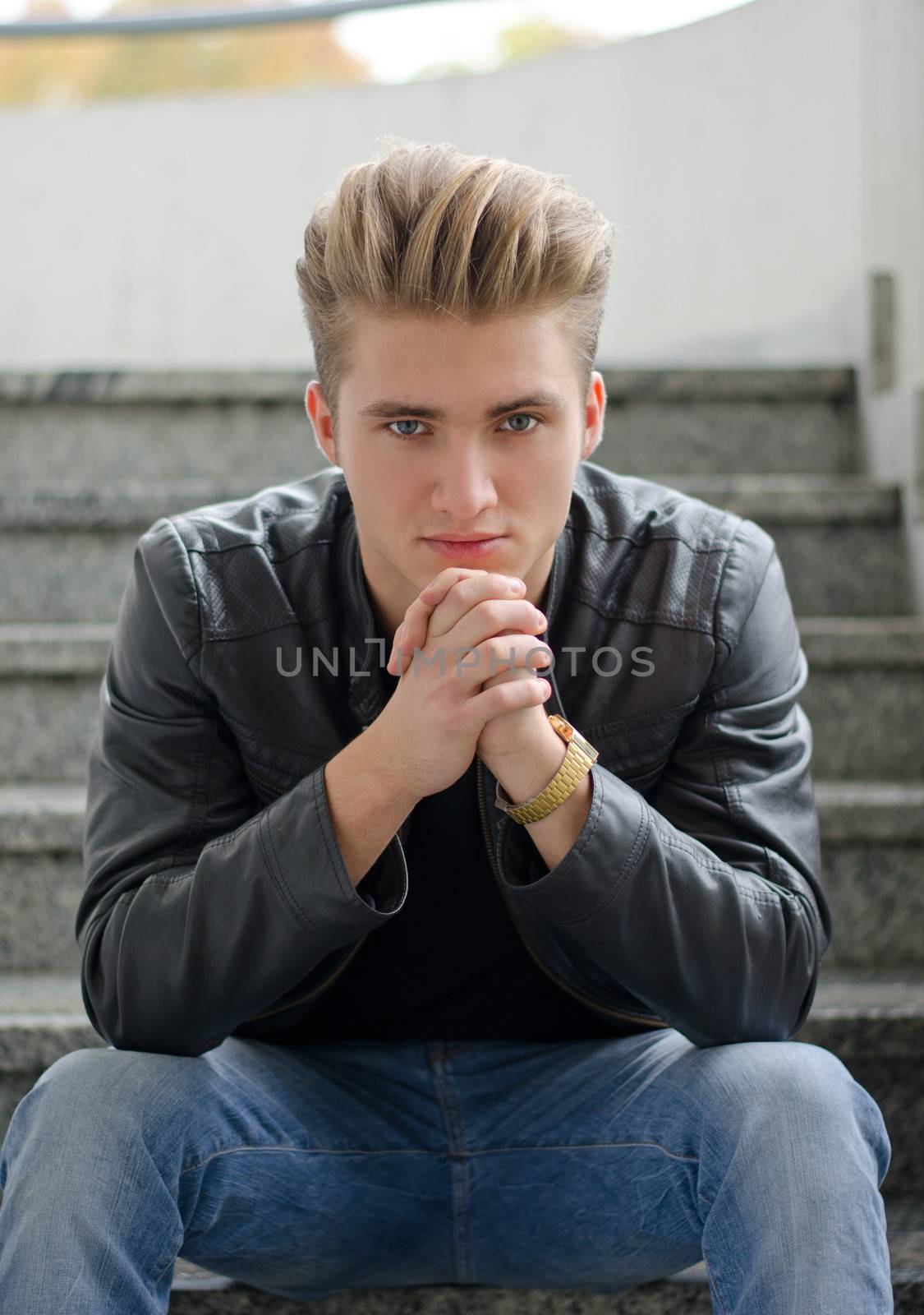 Attractive blond young man, sitting on stairs outdoors looking in camera