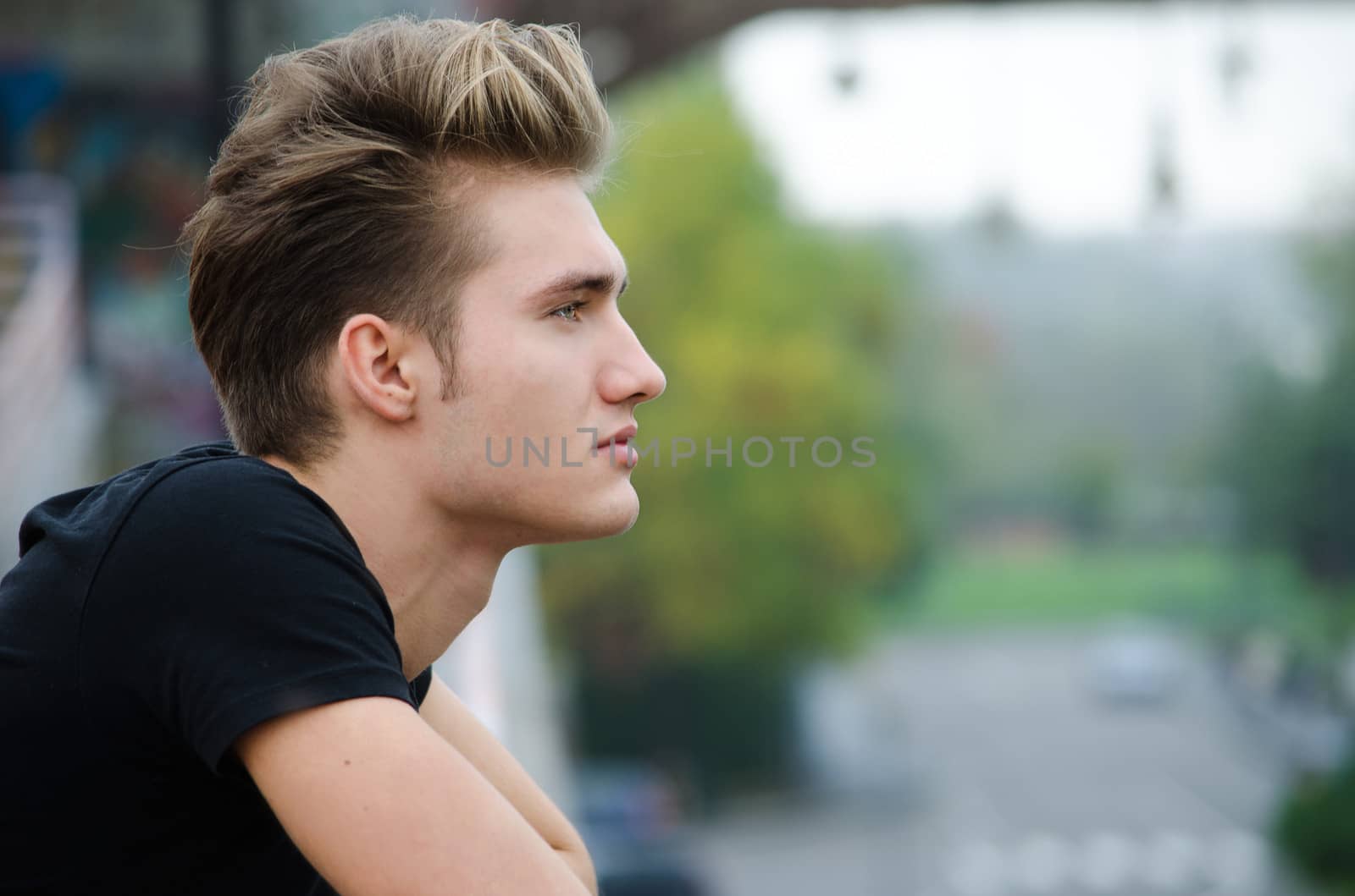 Profile  shot of attractive blond young man in city, looking afar outdoors