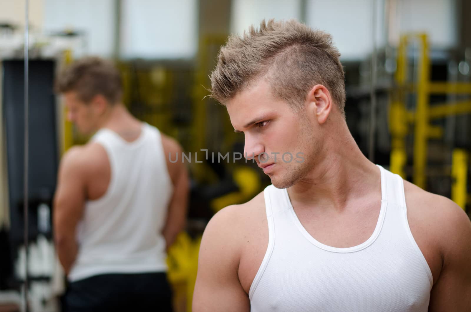 Handsome young man in gym resting and looking down to a side, wearing tanktop