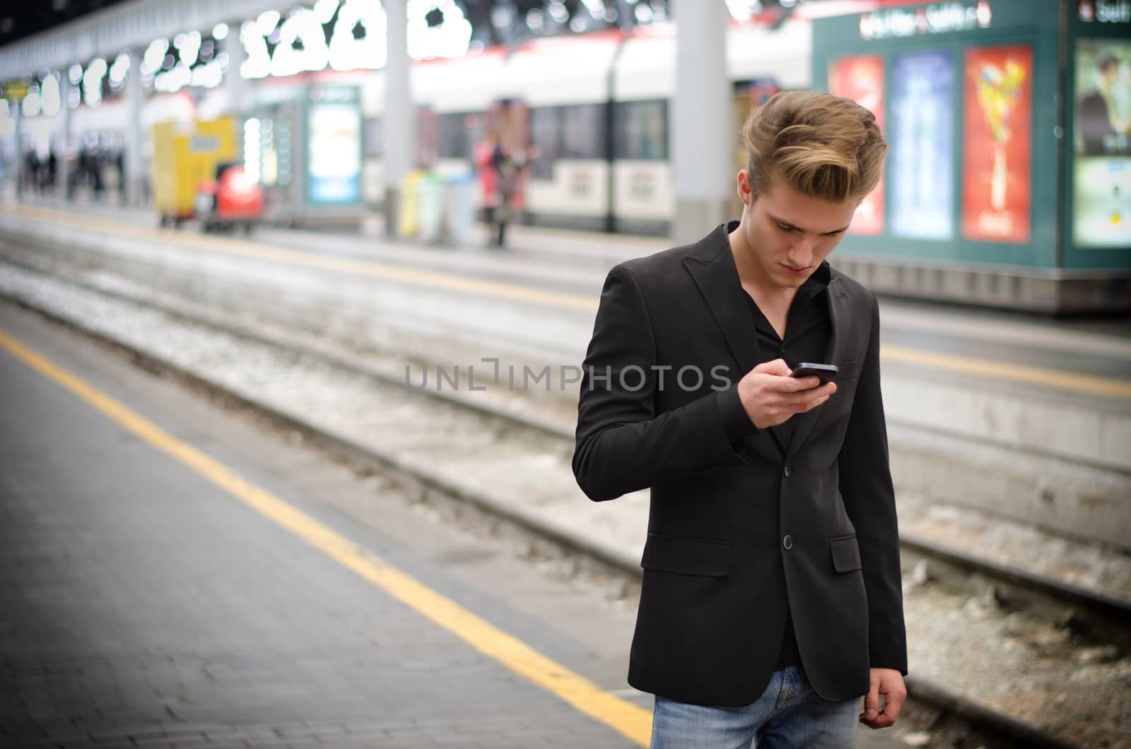 Attractive blond young man in train station using cellphone (mobile)