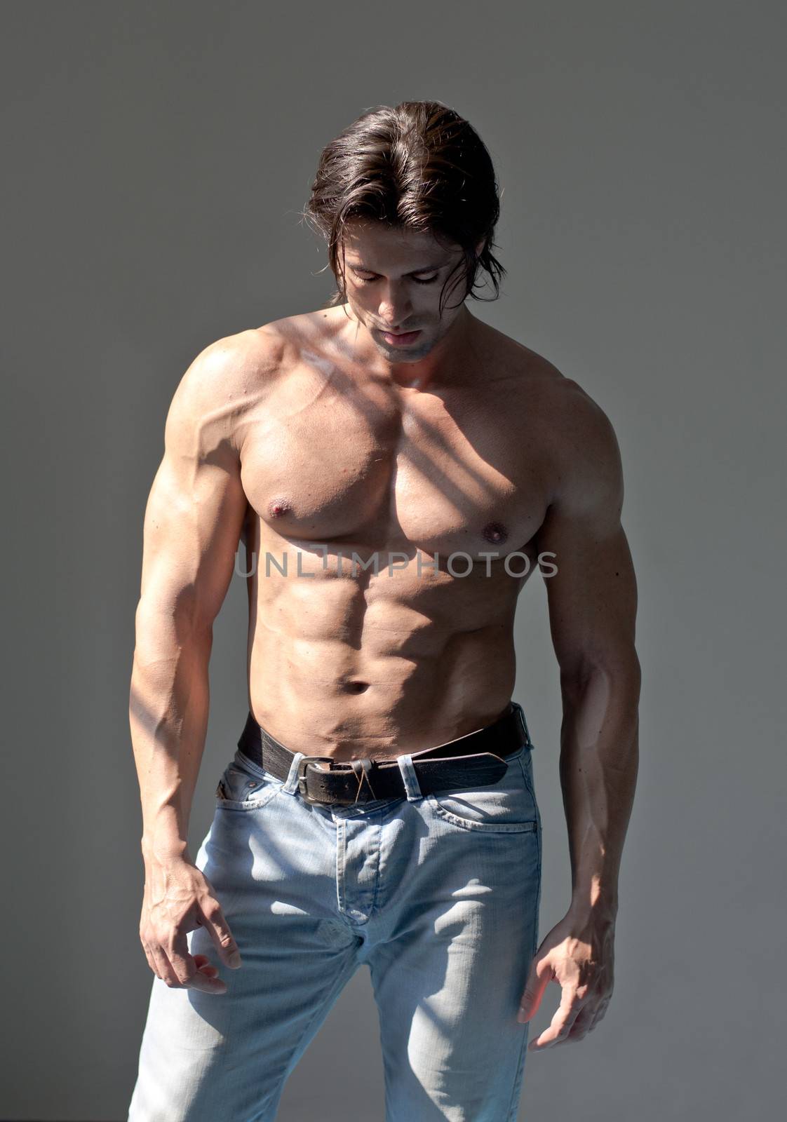 Handsome muscular man shirtless wearing jeans on grey background looking down