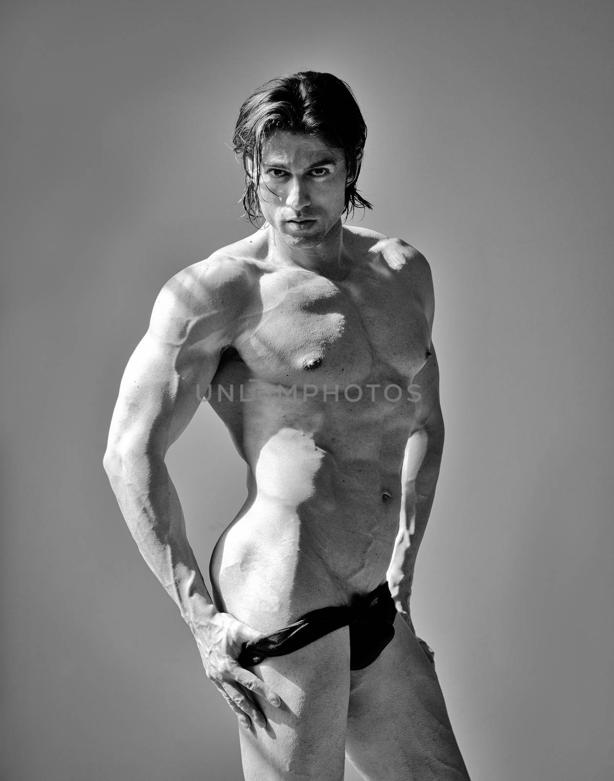 Handsome muscular man shirtless pulling down underwear, on grey background