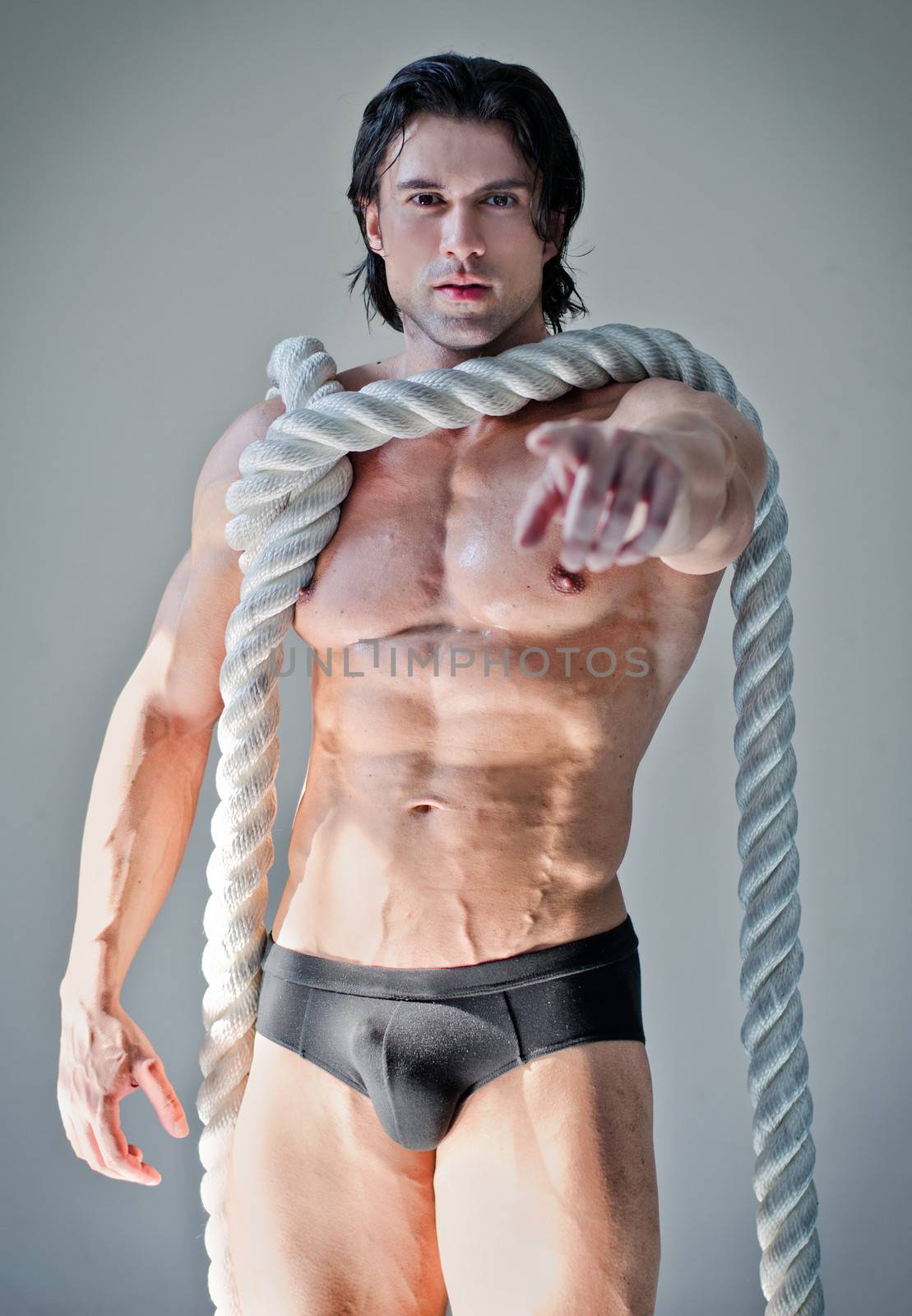 Muscular man in underwear with heavy, big rope around neck, pointing finger at camera