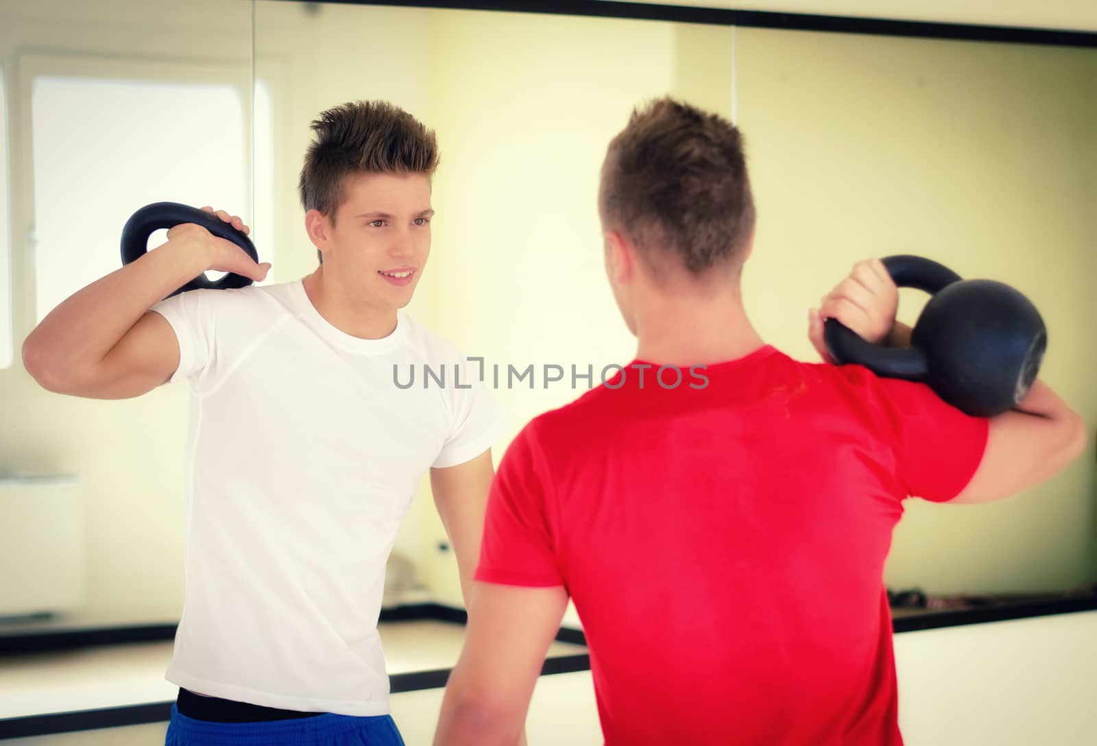 Two handsome young men in gym exercising with kettlebells, smiling