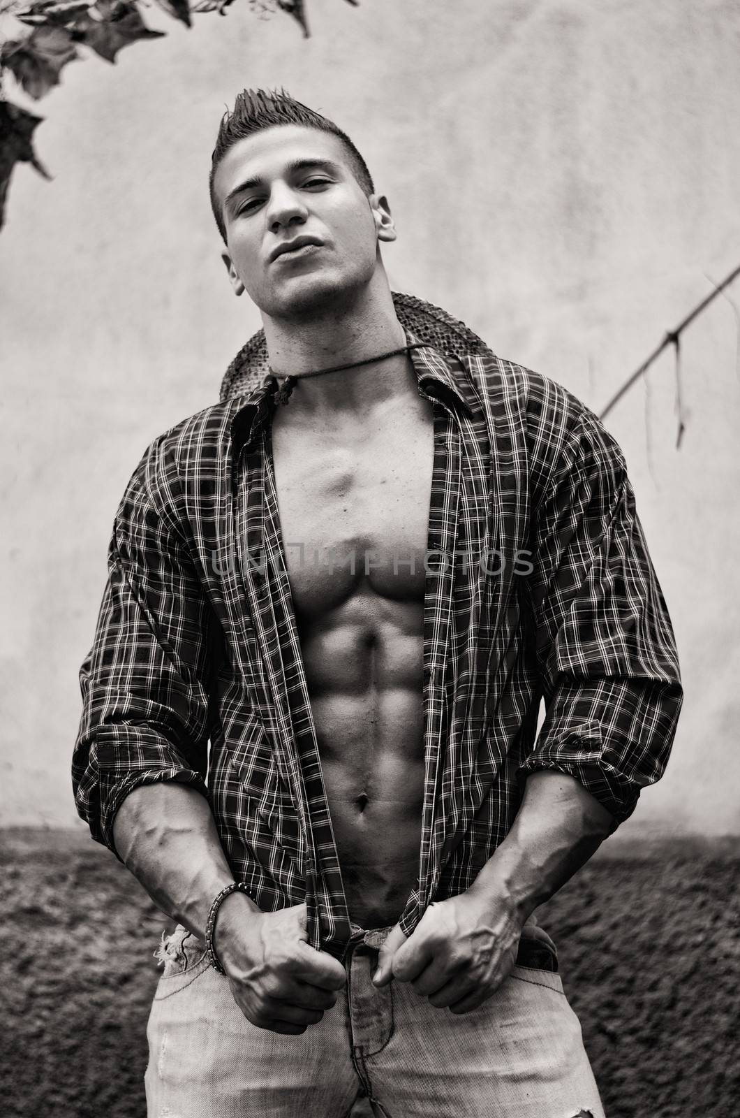 Handsome, muscular young man with open shirt, jeans and straw hat outdoors, black and white shot