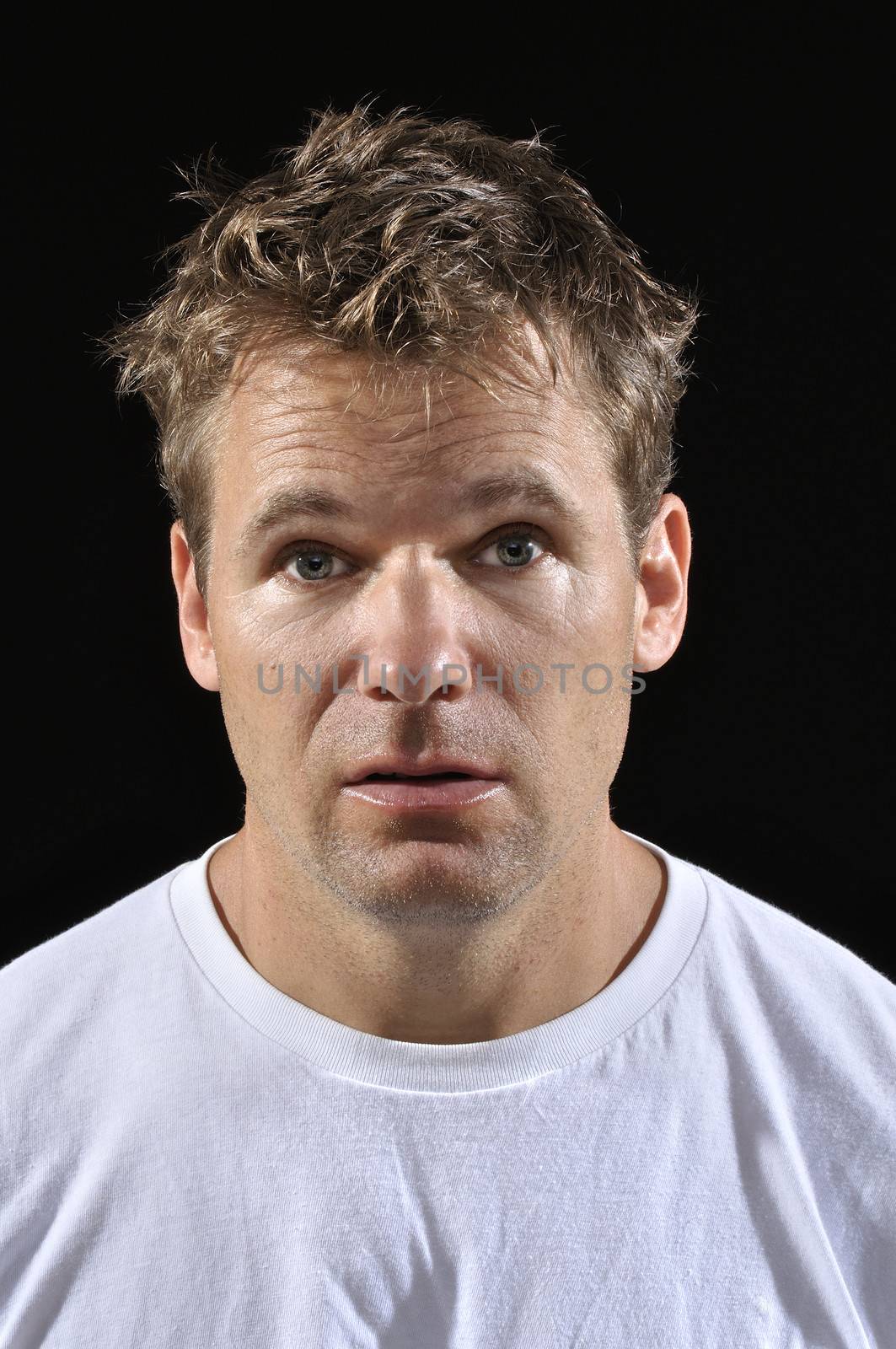 Mug shot of Caucasian man with messy blond hair in white t-shirt on black background