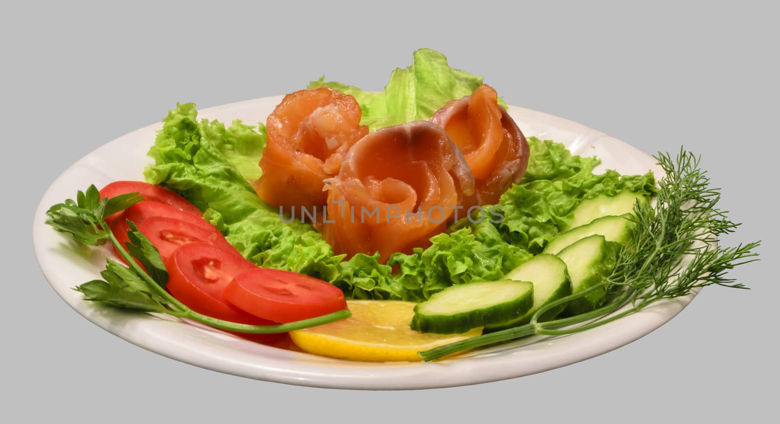 Rolls of red fish fillet with vegetables on the white plate. Isolated on the gray background.