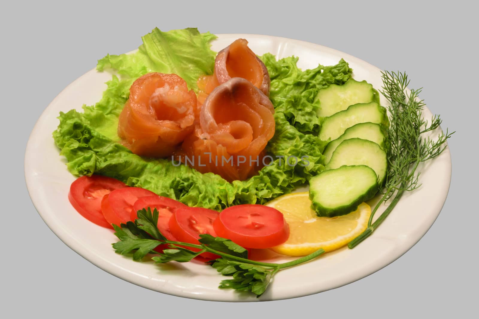 Rolls of red fish fillet with vegetables on the white plate. Isolated on the gray background.