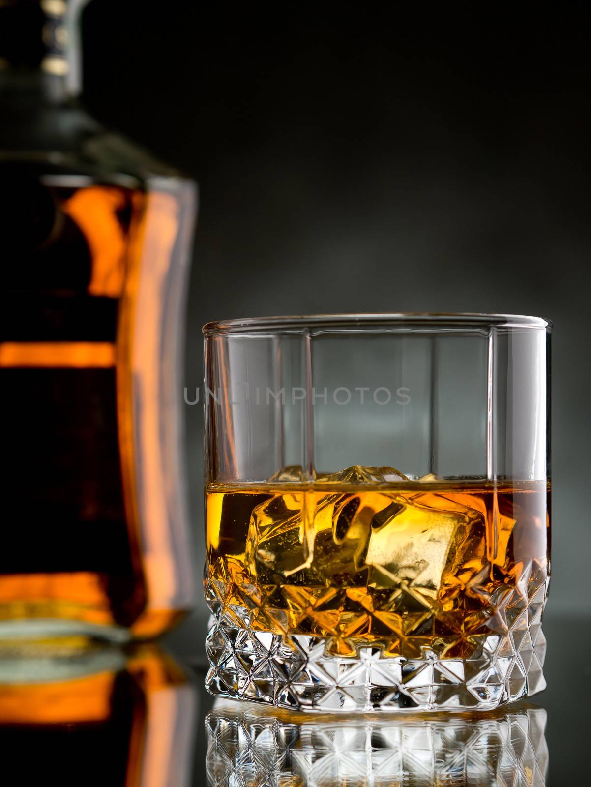 Glass of whisky on the rocks with a bottle