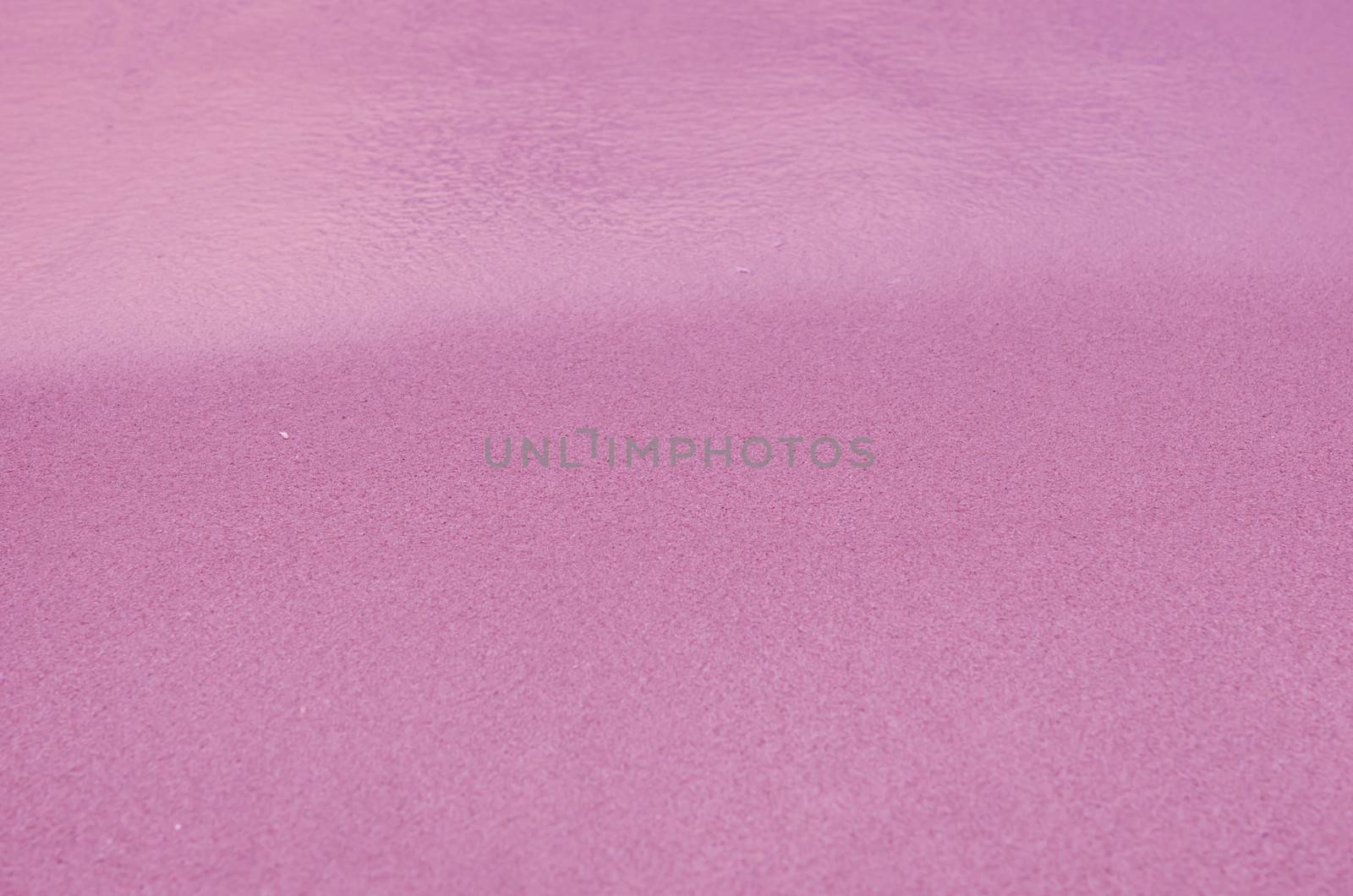 Pink Sandy beach background. Detailed sand texture and water . Top view