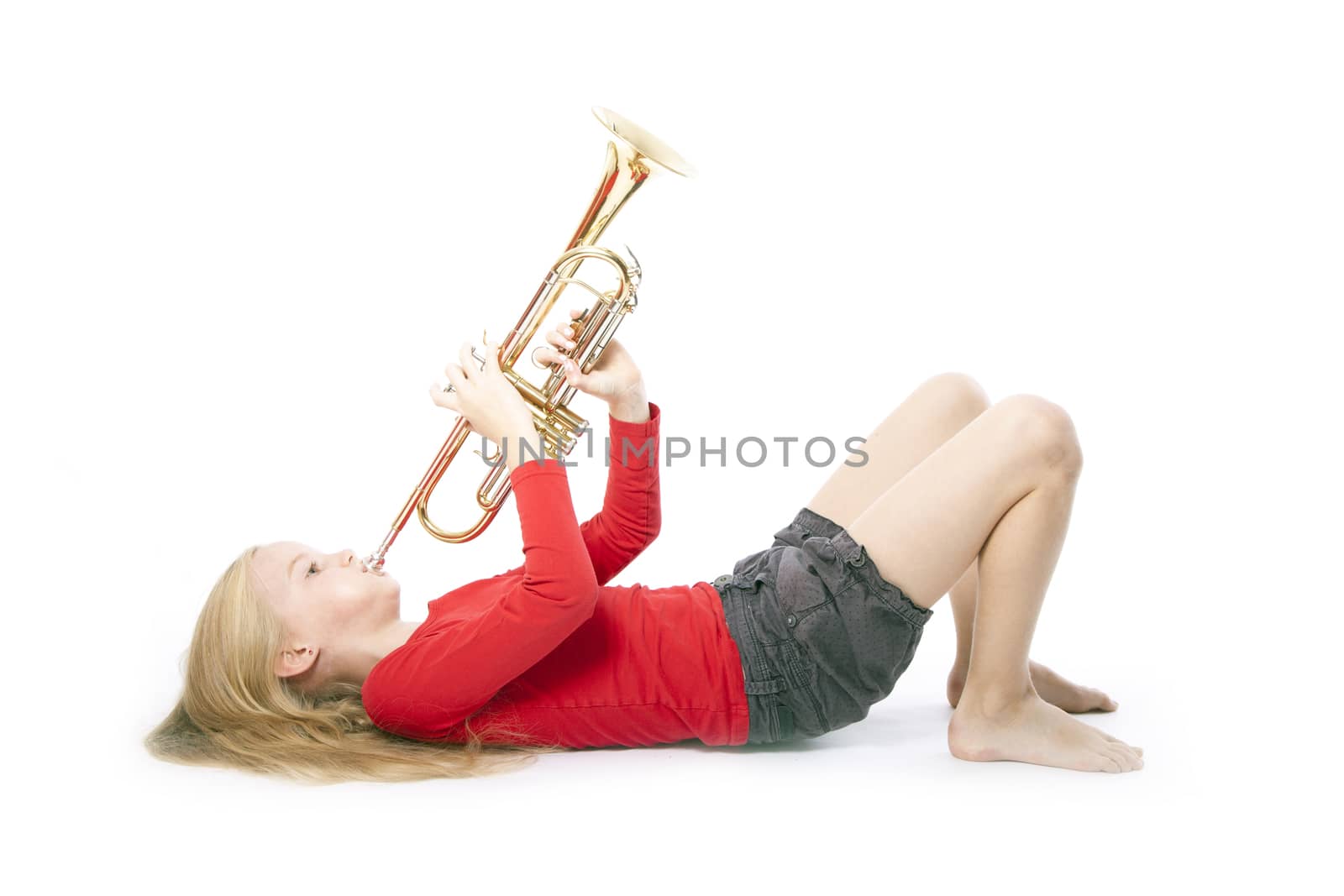young girl in red playing trumpet laying down against white background