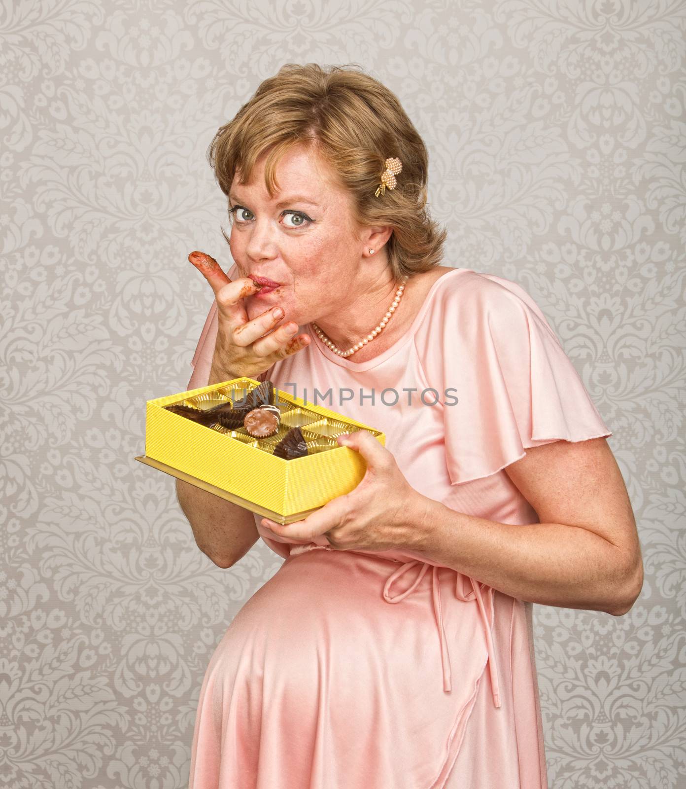Happy expecting woman holding chocolates and licking fingers