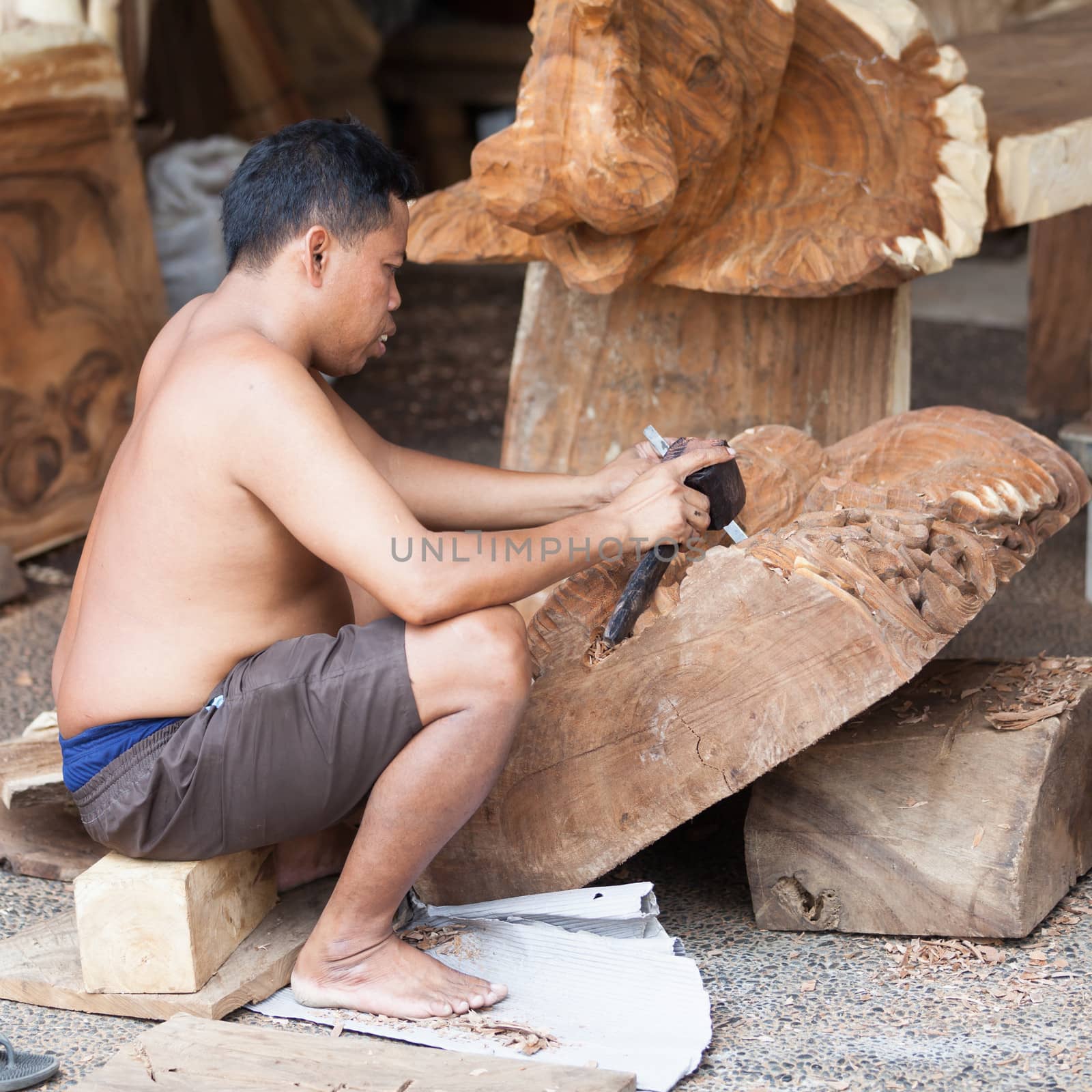 UBUD, BALI, INDONESIA - SEP 21: Balinese carver shapes wood with a chisel and hammer in workshop on Sep 21, 2012 in Ubud, Bali, Indonesia. Balinese handmade souvenirs are popular among tourists.