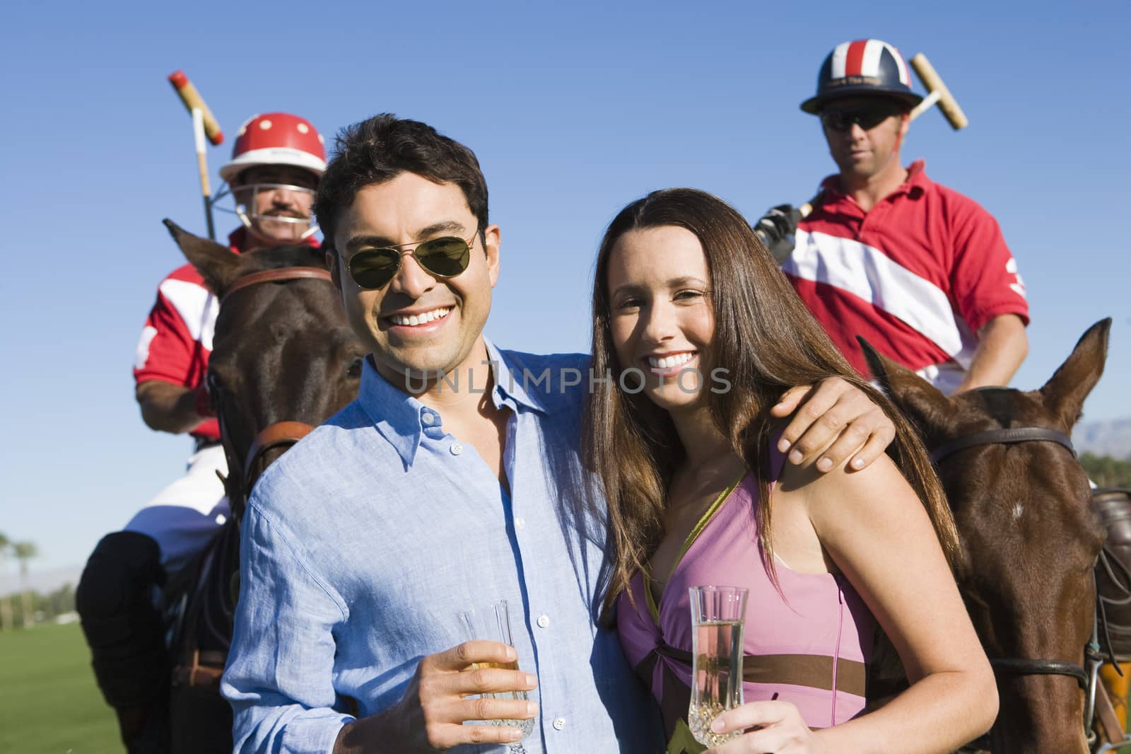 Portrait of happy couple standing with two polo players in the background by moodboard