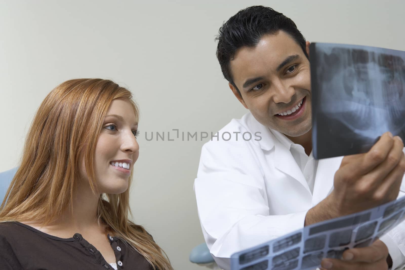 Male dentist and smiling female patient examining r-ray by moodboard