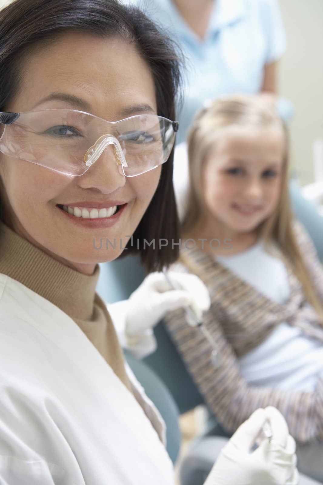 Portrait of a female dentist ready for check-up with little girl sitting in background by moodboard