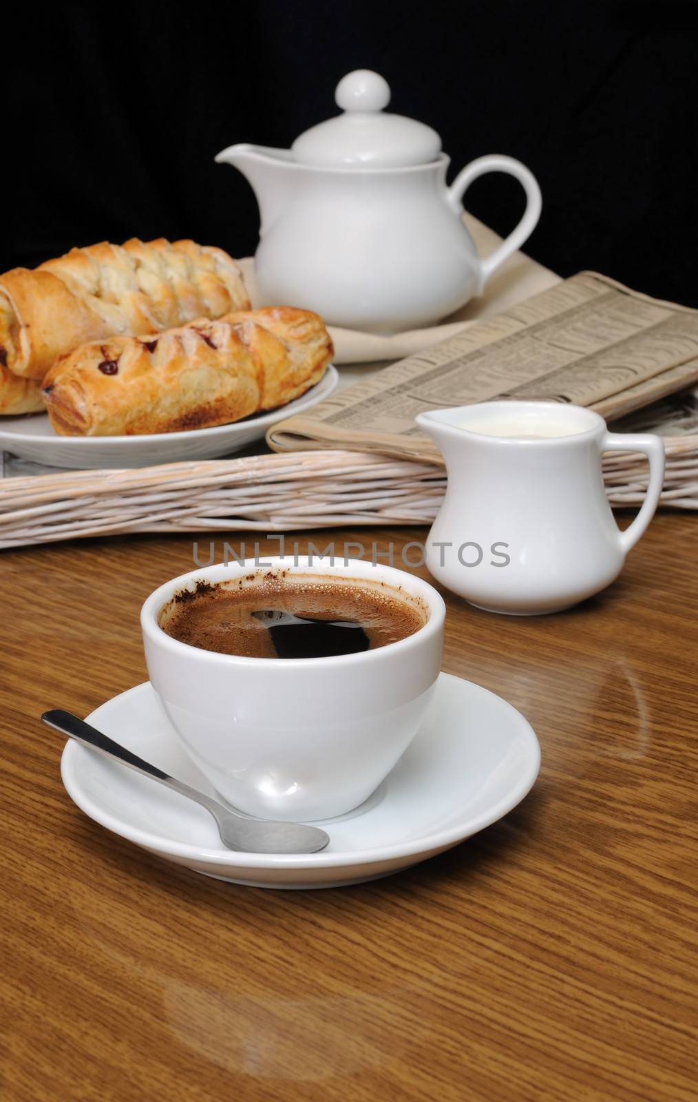 Cup of black coffee on the table with the milkman and biscuits on a tray with newspaper


