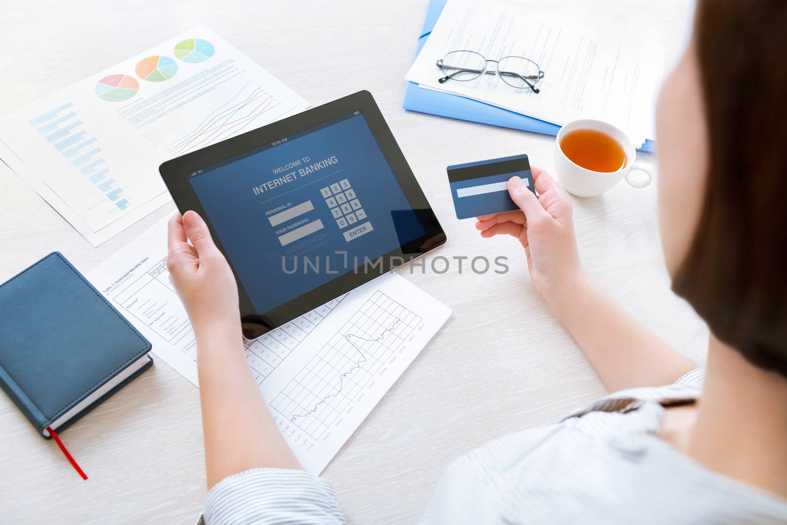 Successful businesswoman sitting at desk in casual clothes and inputting her password and login to carry out online banking operation on digital tablet in the office