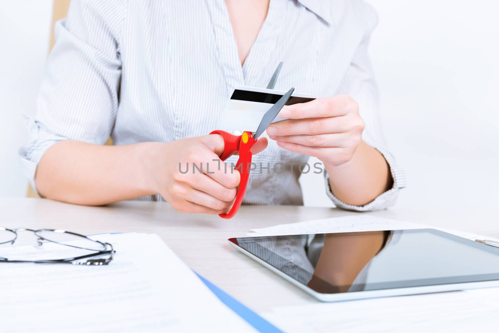 Businesswoman sitting at desk in the office and getting rid of her credit card with the help of scissors after paying back a loan 