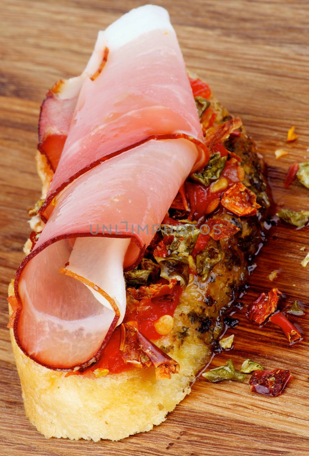 Delicious Spanish Tapas with Cured Ham Prosciutto, Slices of Paprika and Pepper on Toast with Olive Oil closeup on Wooden background