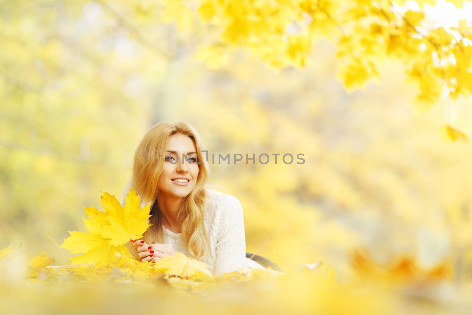 Young woman laying down on the ground covered dry autumnal foliage in beautiful park