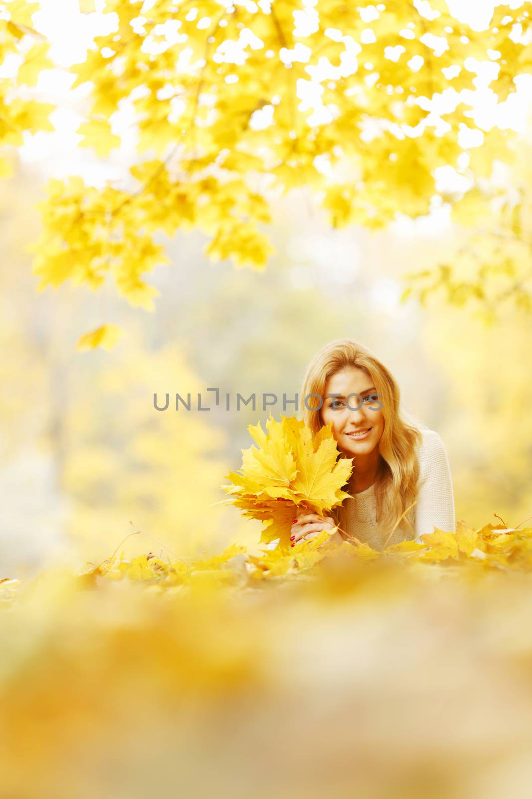 Young woman laying down on the ground covered dry autumnal foliage in beautiful park