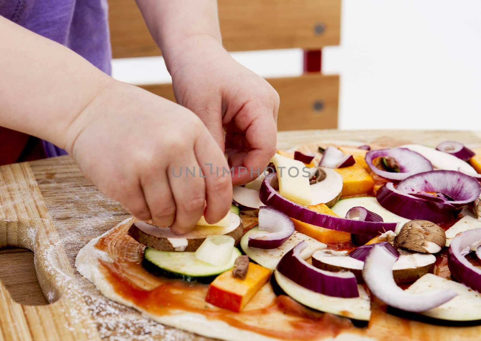 small hands preparing fresh pizza with many vegetables
