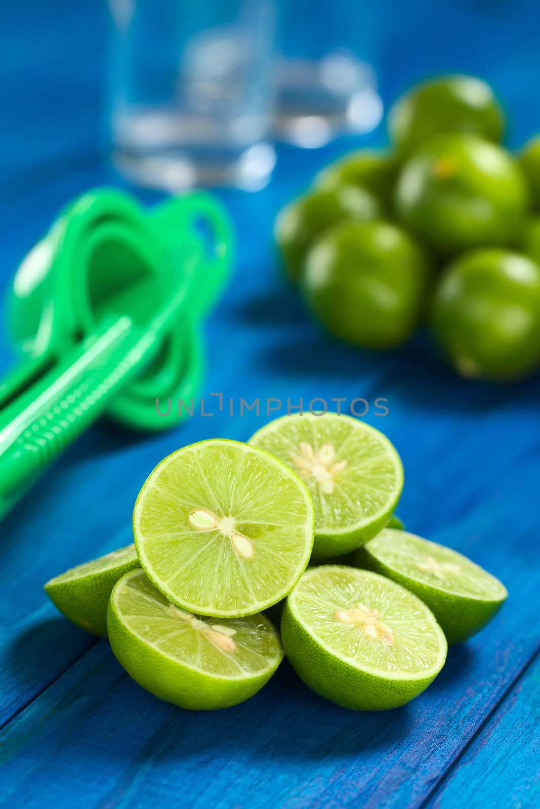 Lime halves on blue wood with squeezer and glasses in the back (Selective Focus, Focus on the lime half on the top) 