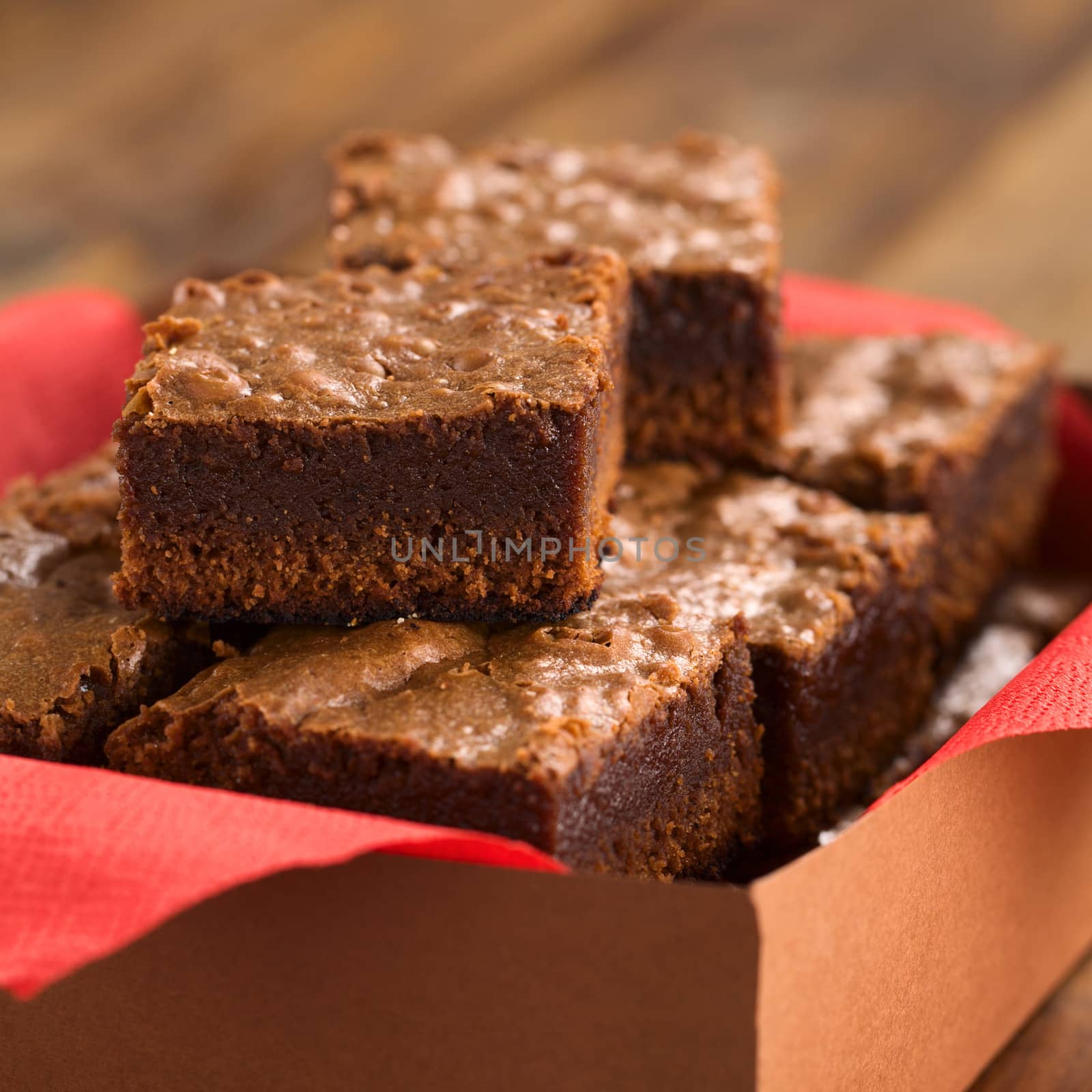 Freshly baked brownies in a brown paper box with red napkin (Selective Focus, Focus on the first brownie on the top)