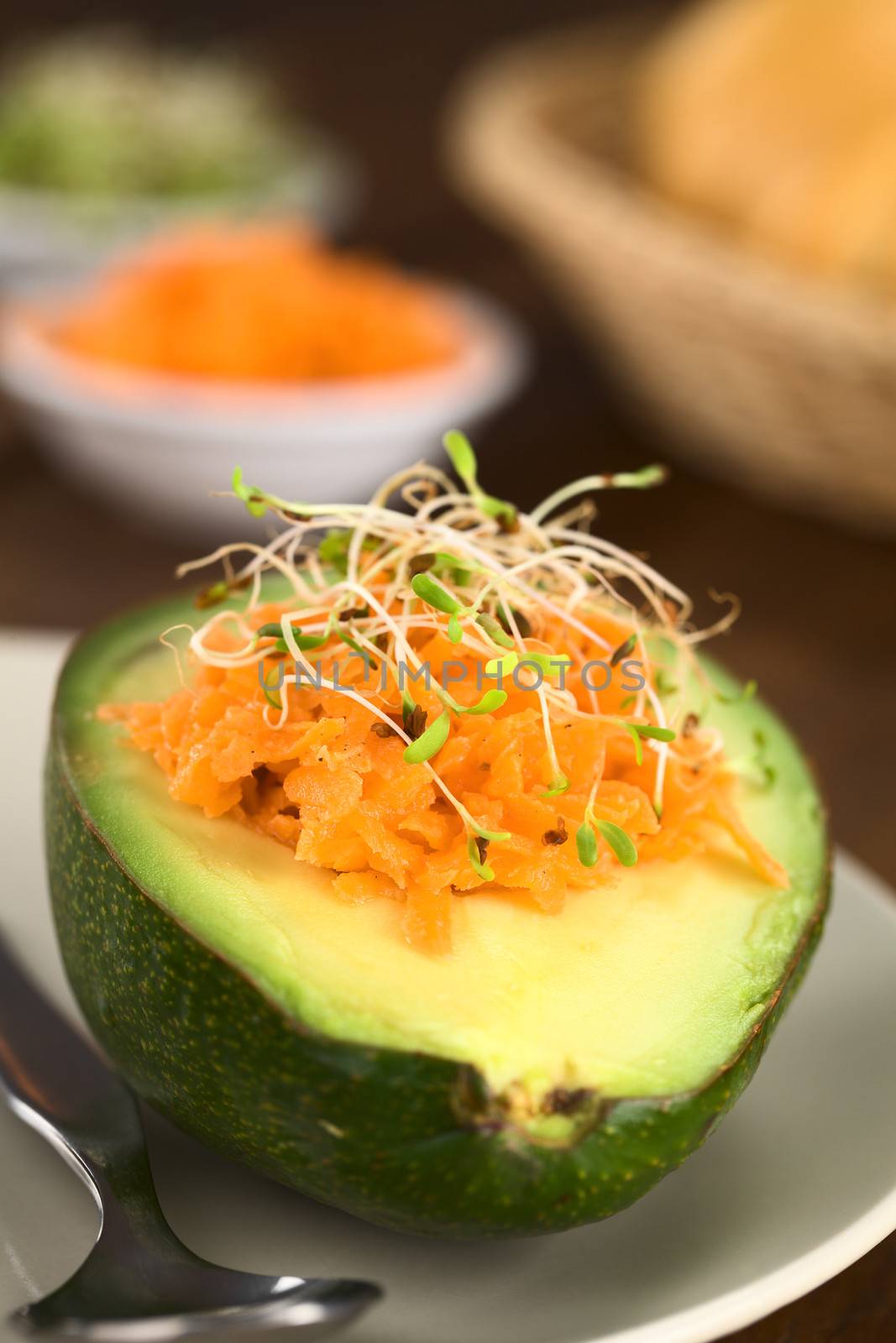 Avocado halves filled with grated carrot and sprinkled with alfalfa sprouts served on plate (Selective Focus, Focus on the front of the grated carrot) 