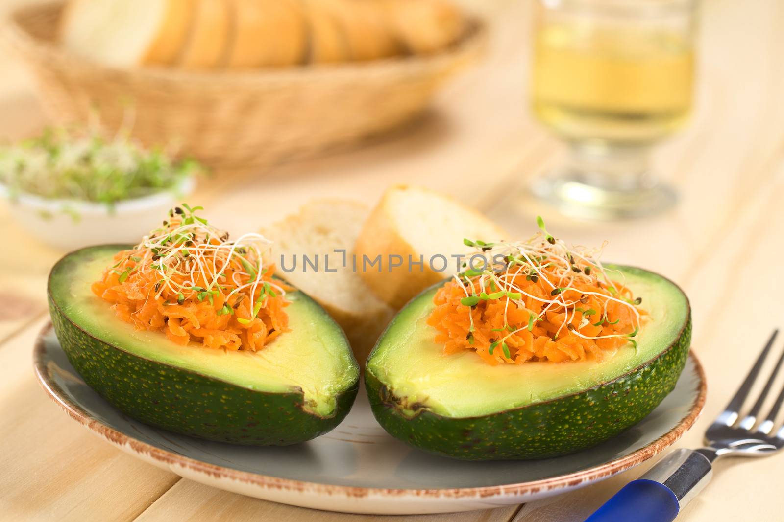 Avocado halves filled with grated carrot and sprinkled with alfalfa sprouts served on plate with baguette slices (Selective Focus, Focus on the front of the grated carrot) 