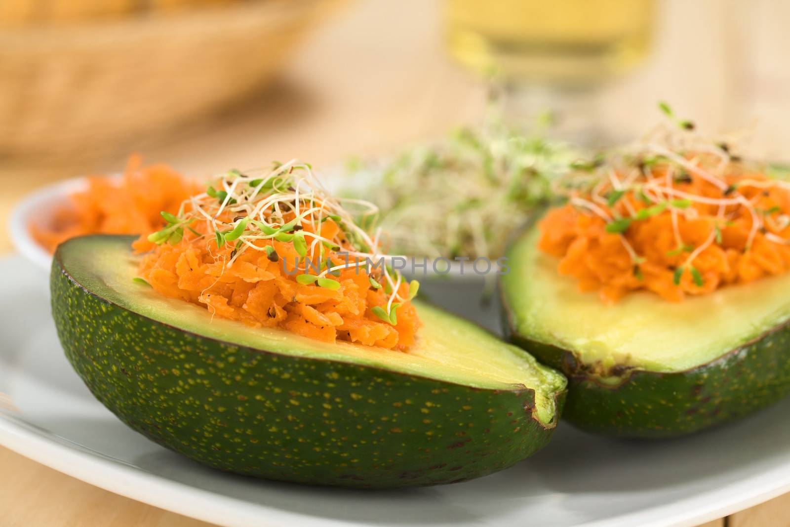 Avocado halves filled with grated carrot and sprinkled with alfalfa sprouts served on plate (Selective Focus, Focus on the front of the grated carrot) 