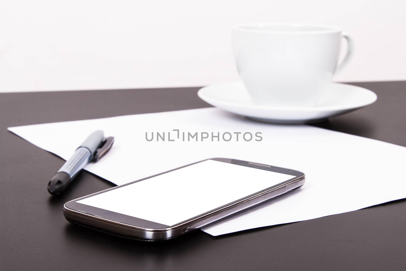 Smart phone with blank, white screen, ceramic coffee cup, pen and empty paper on wooden table, isolated on white background.