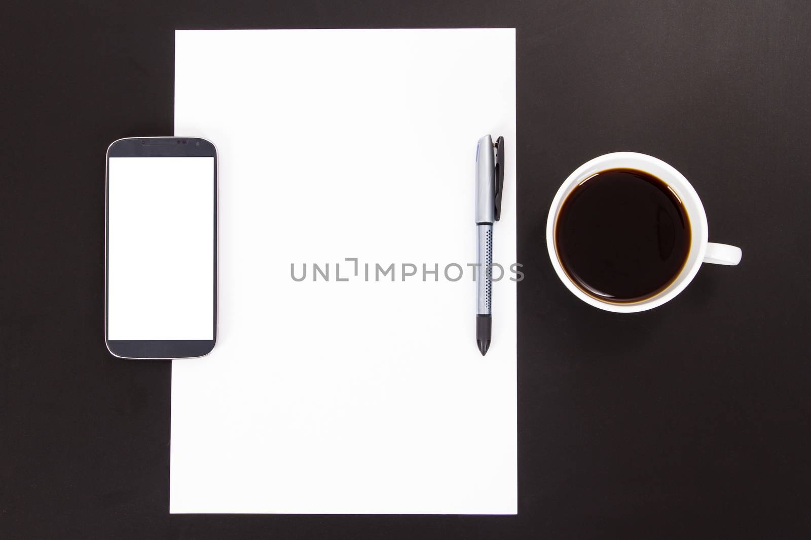 Smart phone with white, blank screen, empty paper, pen and black coffee in white cup on wooden table.