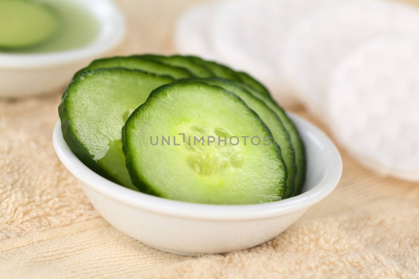 Cucumber slices used as natural moisturizer pads for the eyes in a bowl on towel (Selective Focus, Focus on the middle of the first cucumber slice)