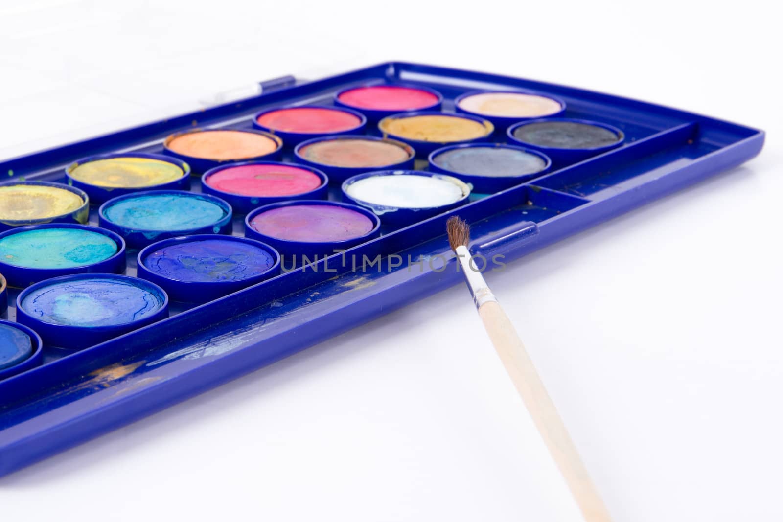 Close up of messy water color paint box and thin brush, isolated on white.